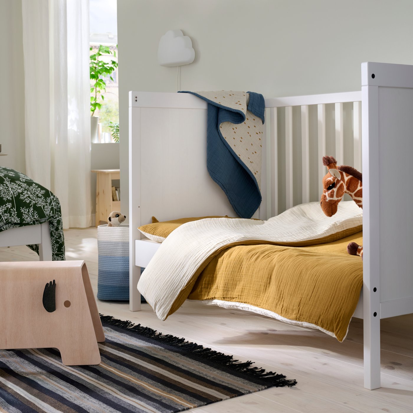 A child’s SUNDVIK cot in a family bedroom with a brown quilt and a giraffe toy.