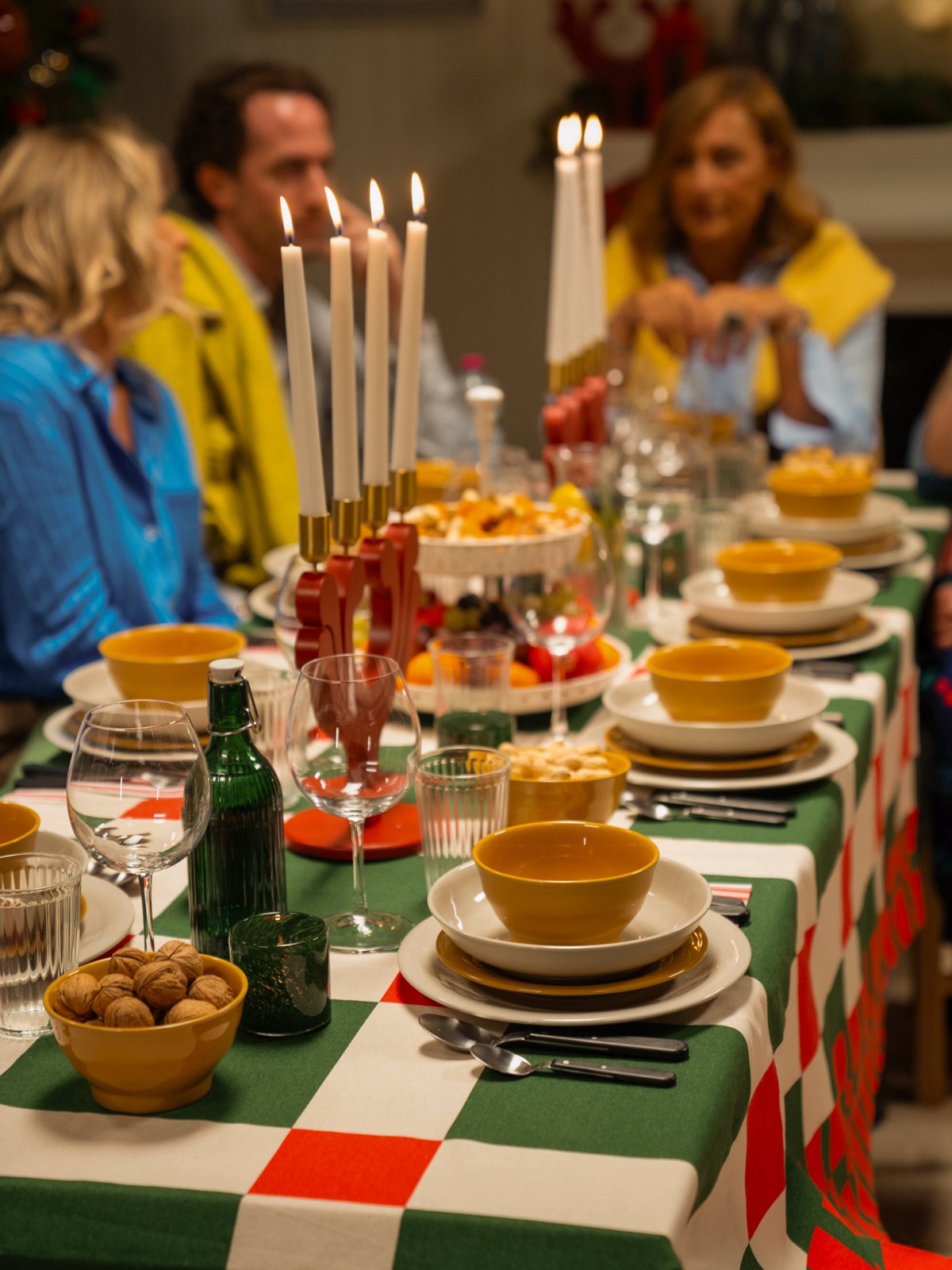 Una tavola imbandita per le feste con una tovaglia a scacchi verdi e bianchi, ciotole gialle STRIMMIG e un candelabro rosso VINTERFINT con candele accese.