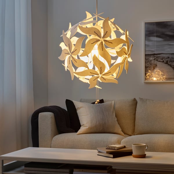 A white RAMSELE pendant lamp hangs in a living room near a sofa with a throw hanging over one end. The lamp is lit.