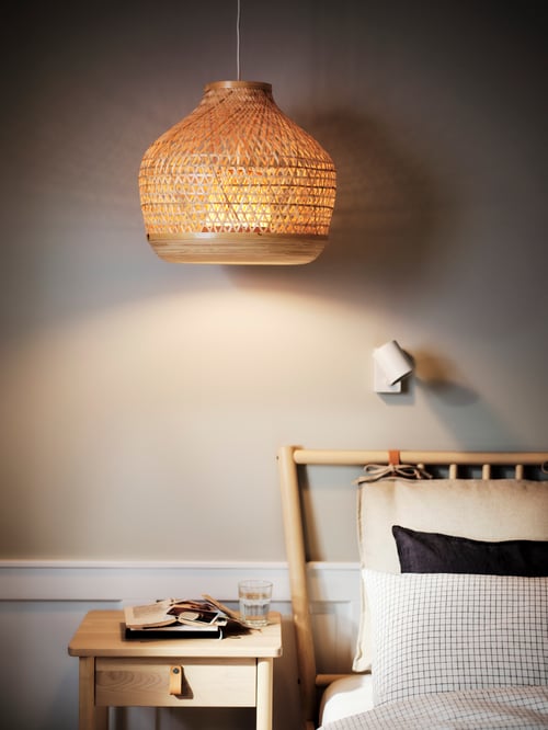 Bedroom area featuring a lit pendant lamp hanging over a bedside table, and a bed with multiple cushions.