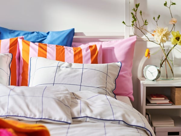 Close-up of bed with a lot of pillows in different patterns and colours. Bedside table on the right.