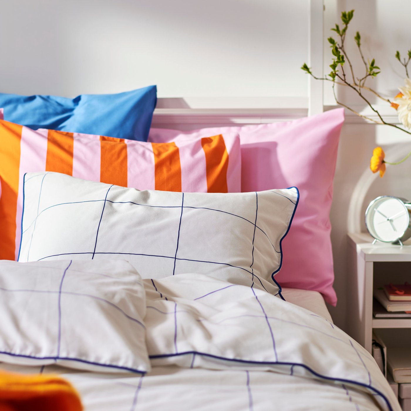 Close-up of bed with a lot of pillows in different patterns and colours. Bedside table on the right.