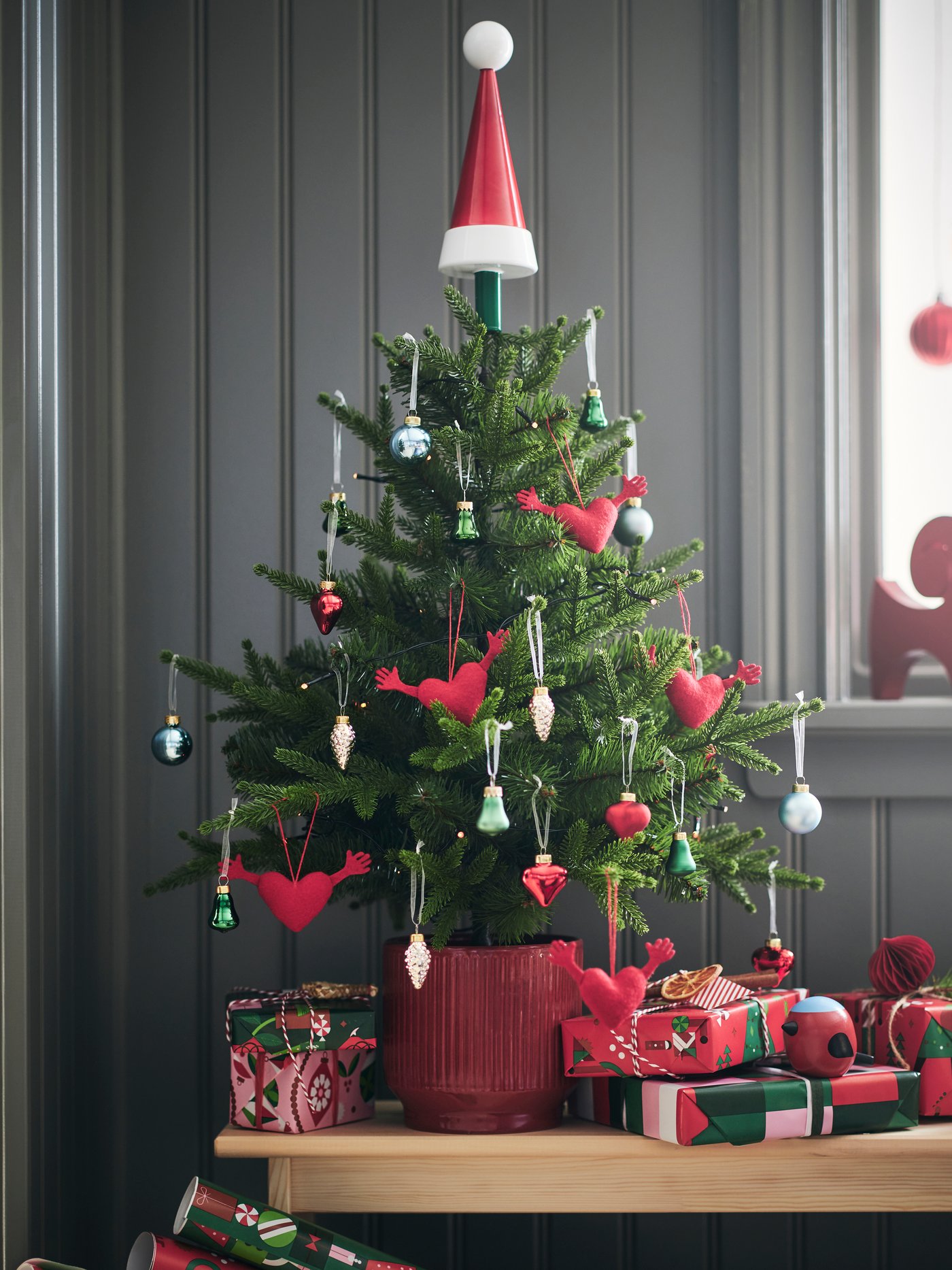 Un piccolo albero di Natale in vaso è decorato con allegri ornamenti VINTERFINT e posizionato su una panca con dei regali.