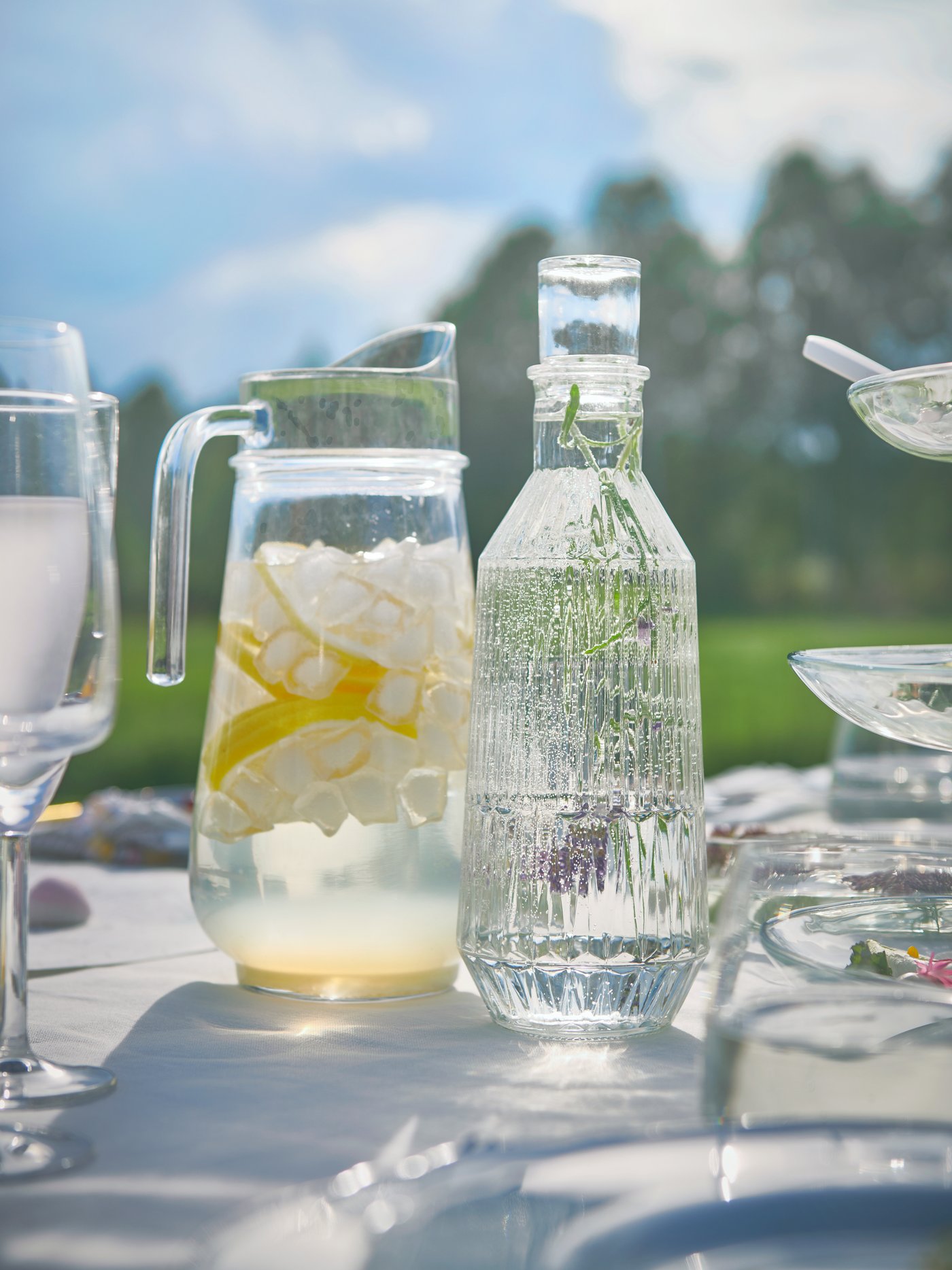 Una mesa con una botella y un jarro de vidrio encima. Ambos tienen líquidos refrescantes en su interior.