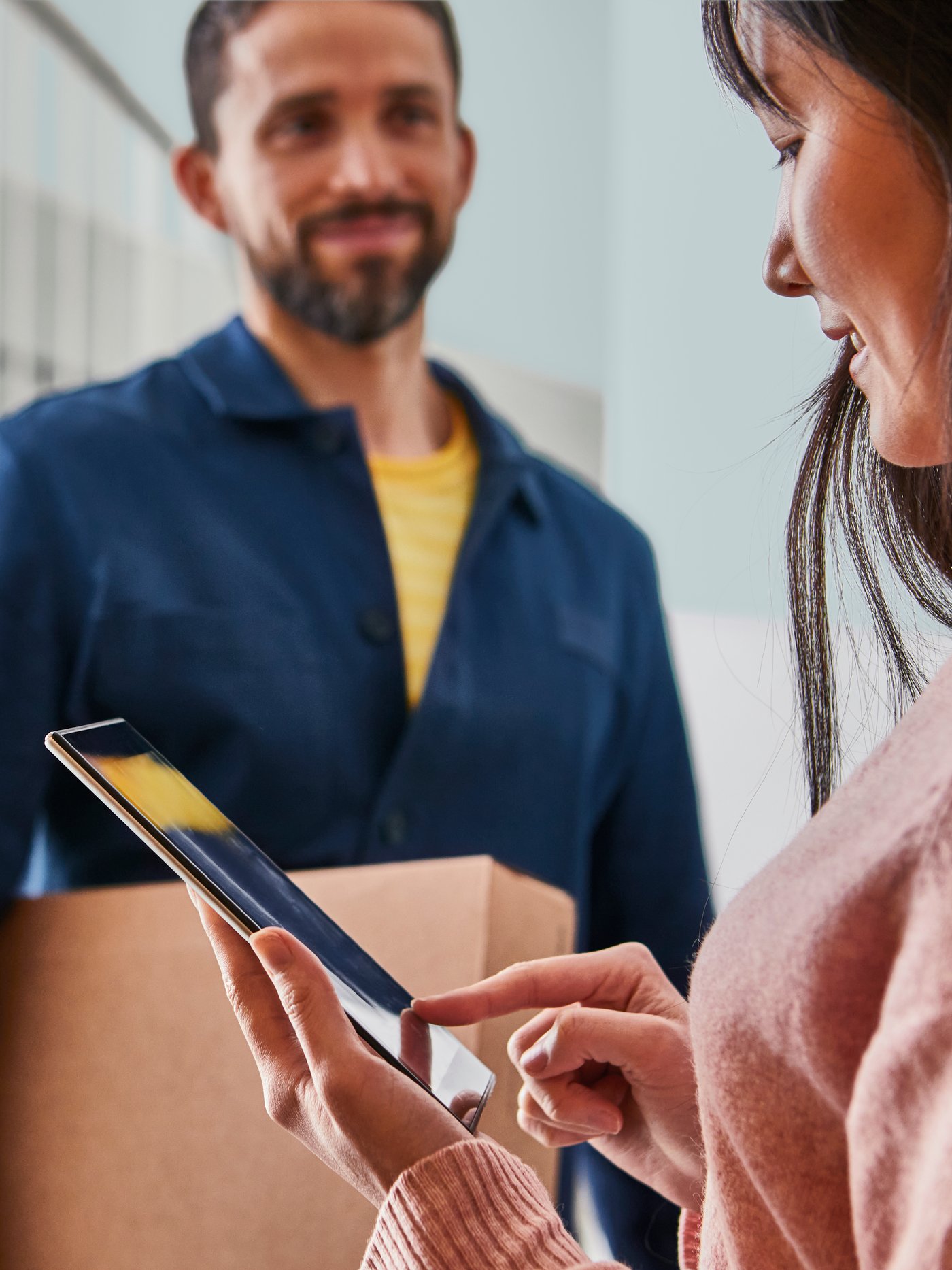 Zwei Personen in einem Hausflur. Eine Person bringt der anderen ein Paket.