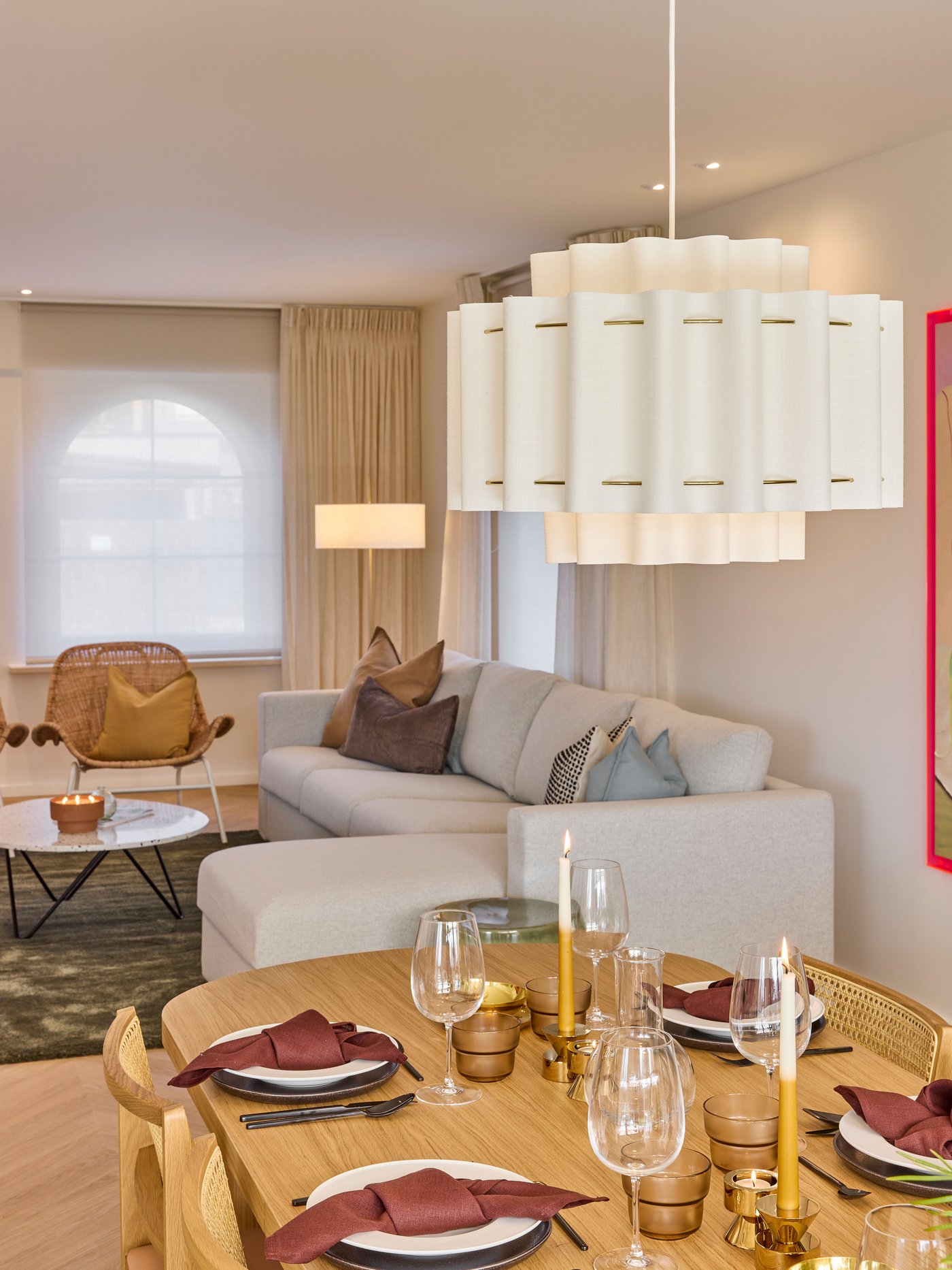 Open leefruimte met sofa, eettafel, stoelen en hanglamp in zachte, neutrale tinten.