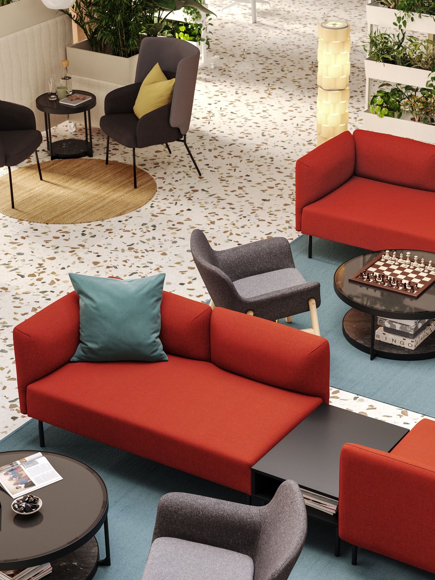 An aerial view of a hotel lobby with two seating areas defined by red LILLEHEM modular sofas and grey armchairs on big rugs.