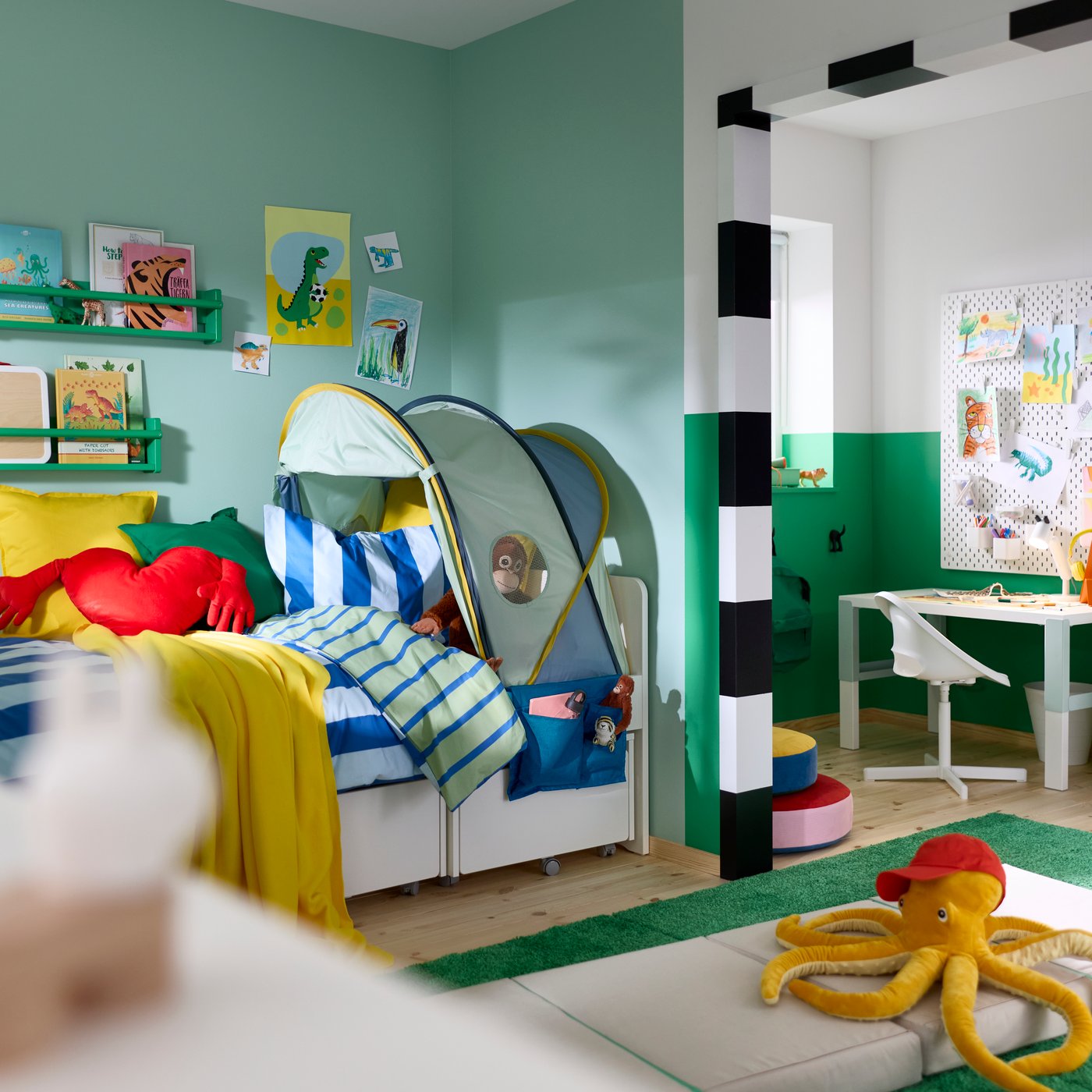 An ELDFLUGA bed tent mounted over a children’s bed with bedding and toys in a room with green walls and decorations.