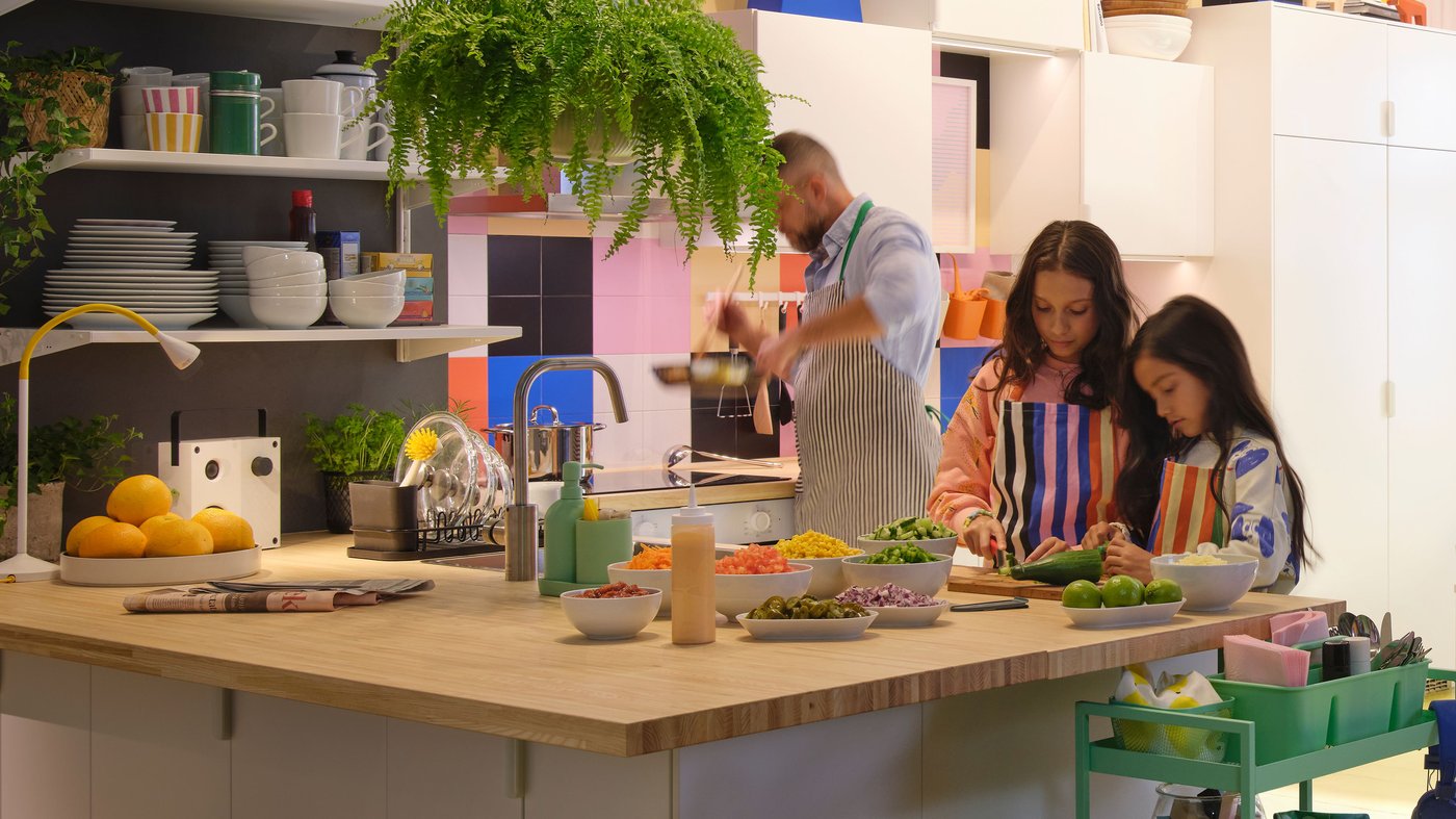 キッチンのアイランドカウンターで、カラフルなエプロンを着た子どもと大人が食材を切り分ける、イケアのリビング＆ダイニング空間