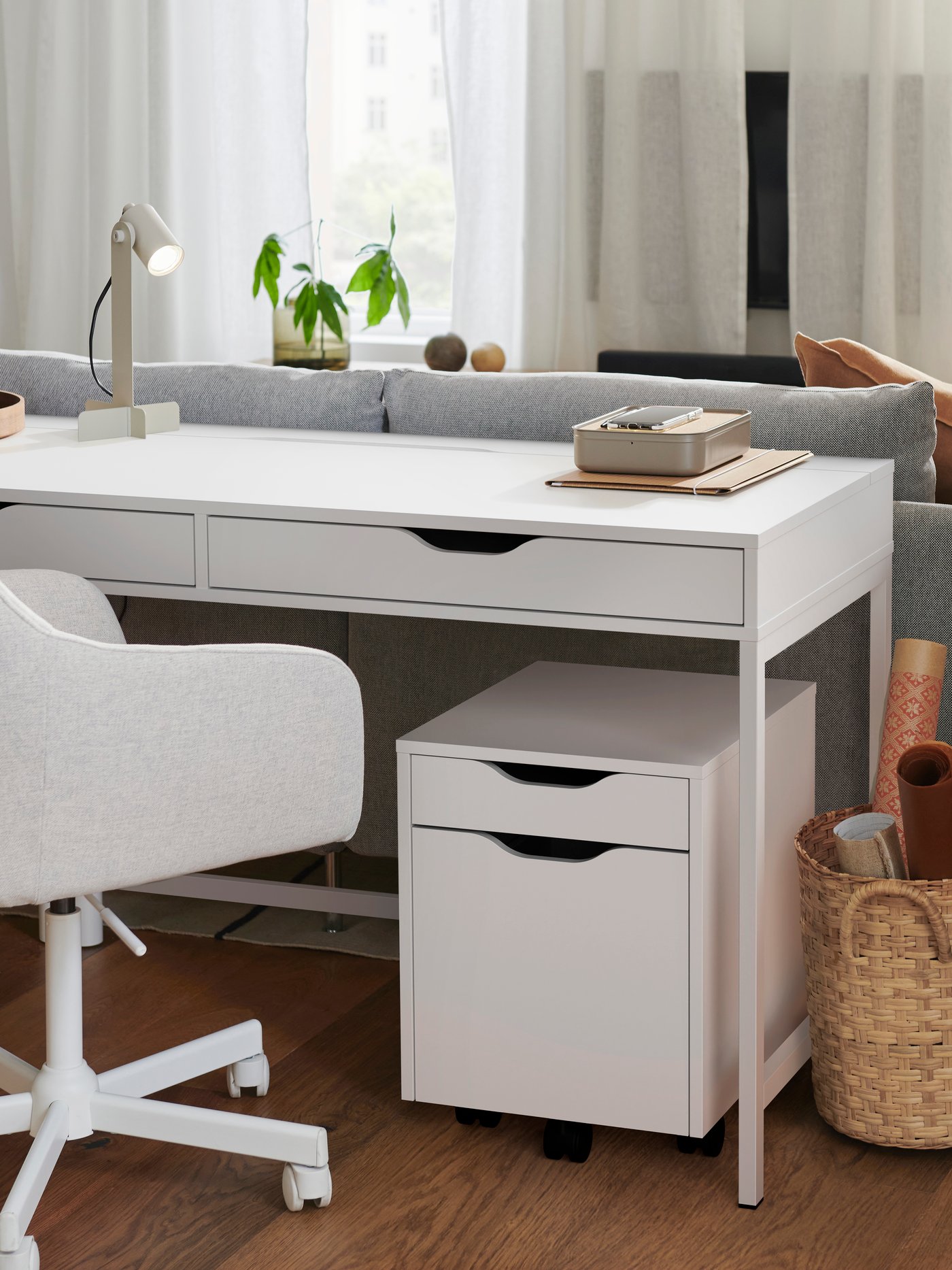A white ALEX desk with drawers in a living room, with a white desk chair and ALEX drawer unit on castors