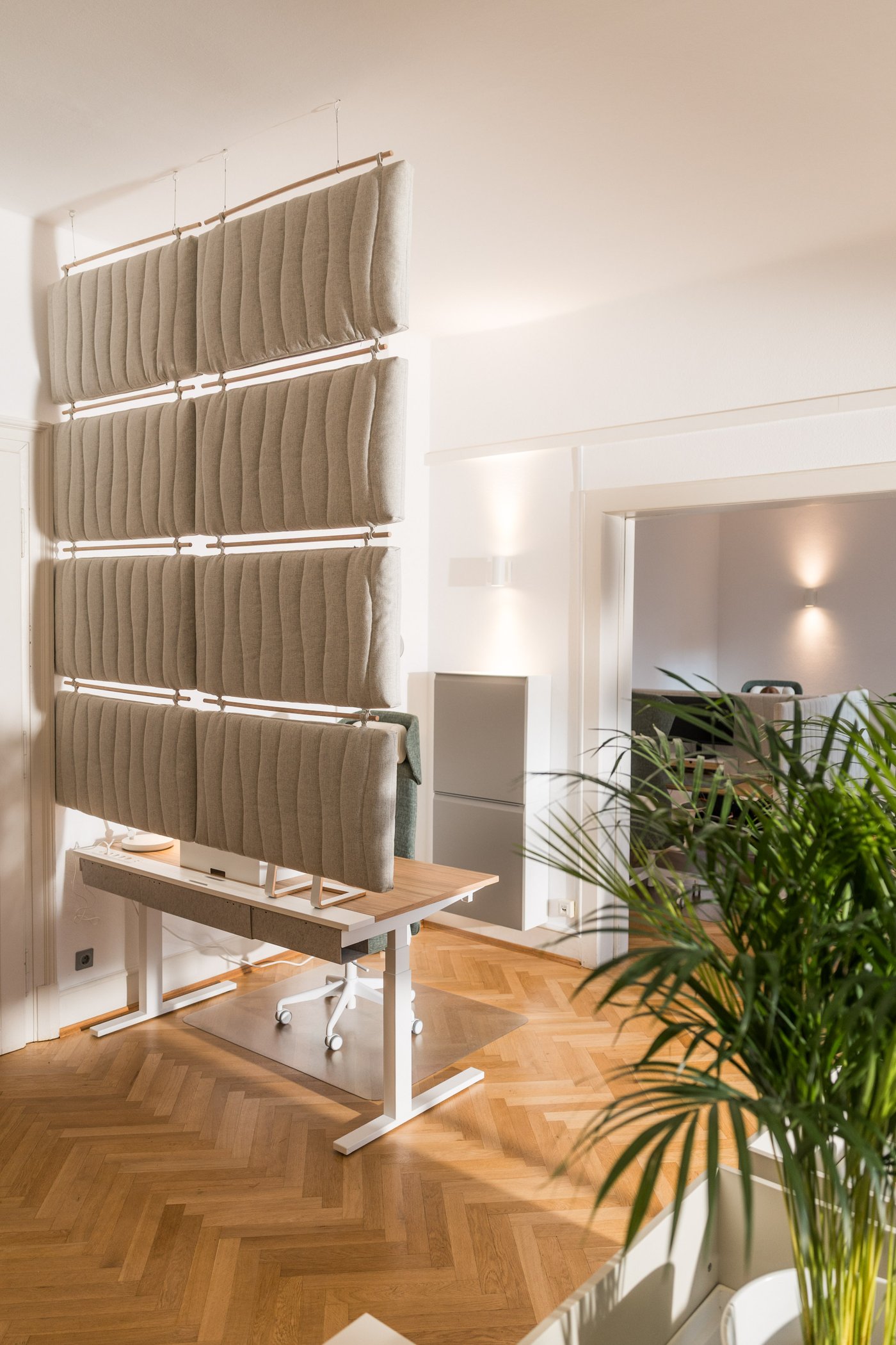 Freistehendes Element mit mehreren vertikalen Akustik-Paneelen in einem Büro mit Parkettboden und Pflanzen.