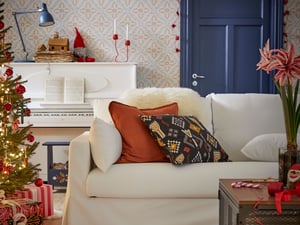 O față de pernă DYTÅG de culoare roșu-maro pe o canapea HYLARP așezată într-o cameră de zi, lângă un brad de Crăciun.