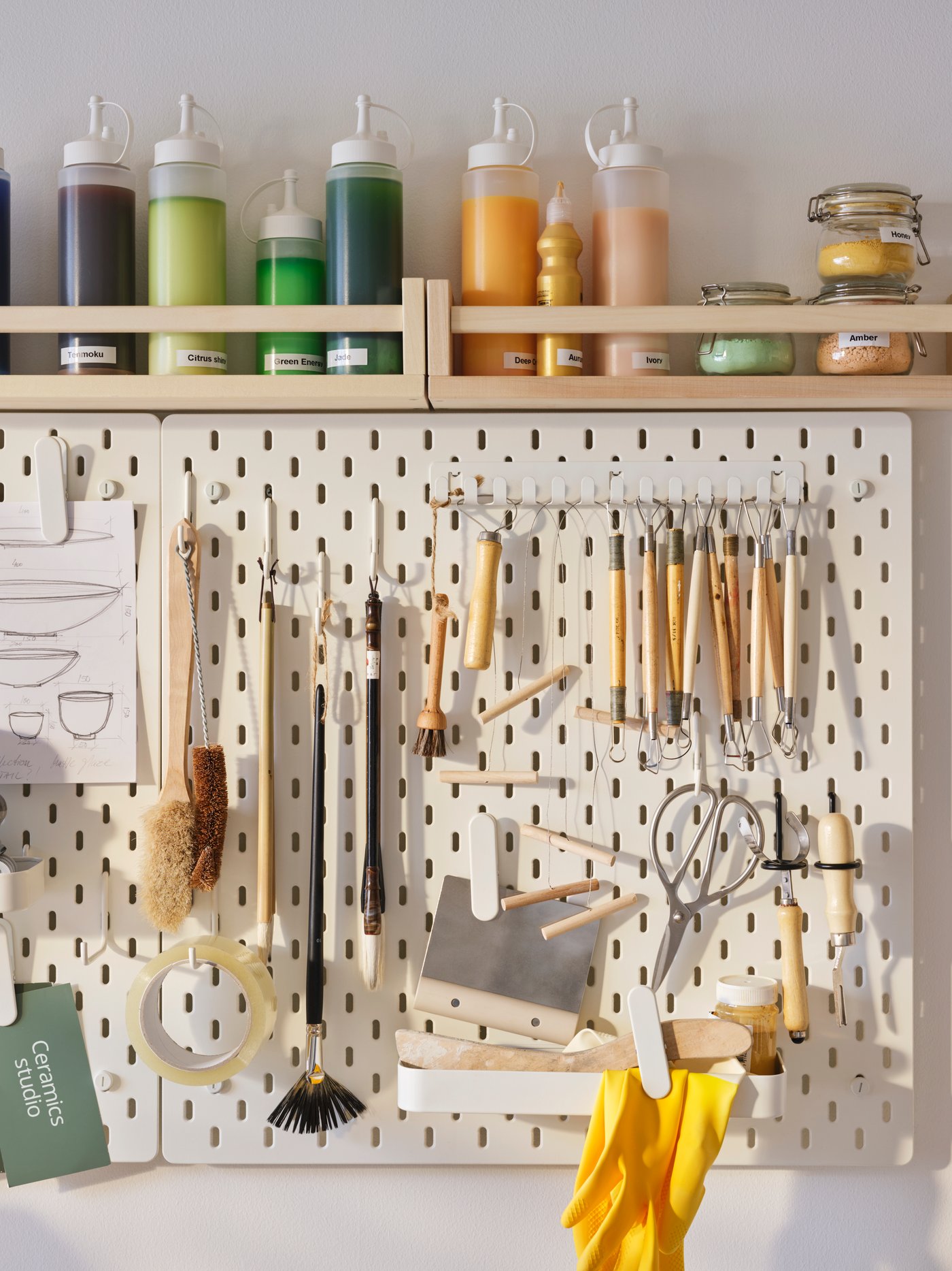 A wall storage solution comprised of a SKÅDIS pegboard for pottery tools and a BEKVÄM spice rack for storing glazes.