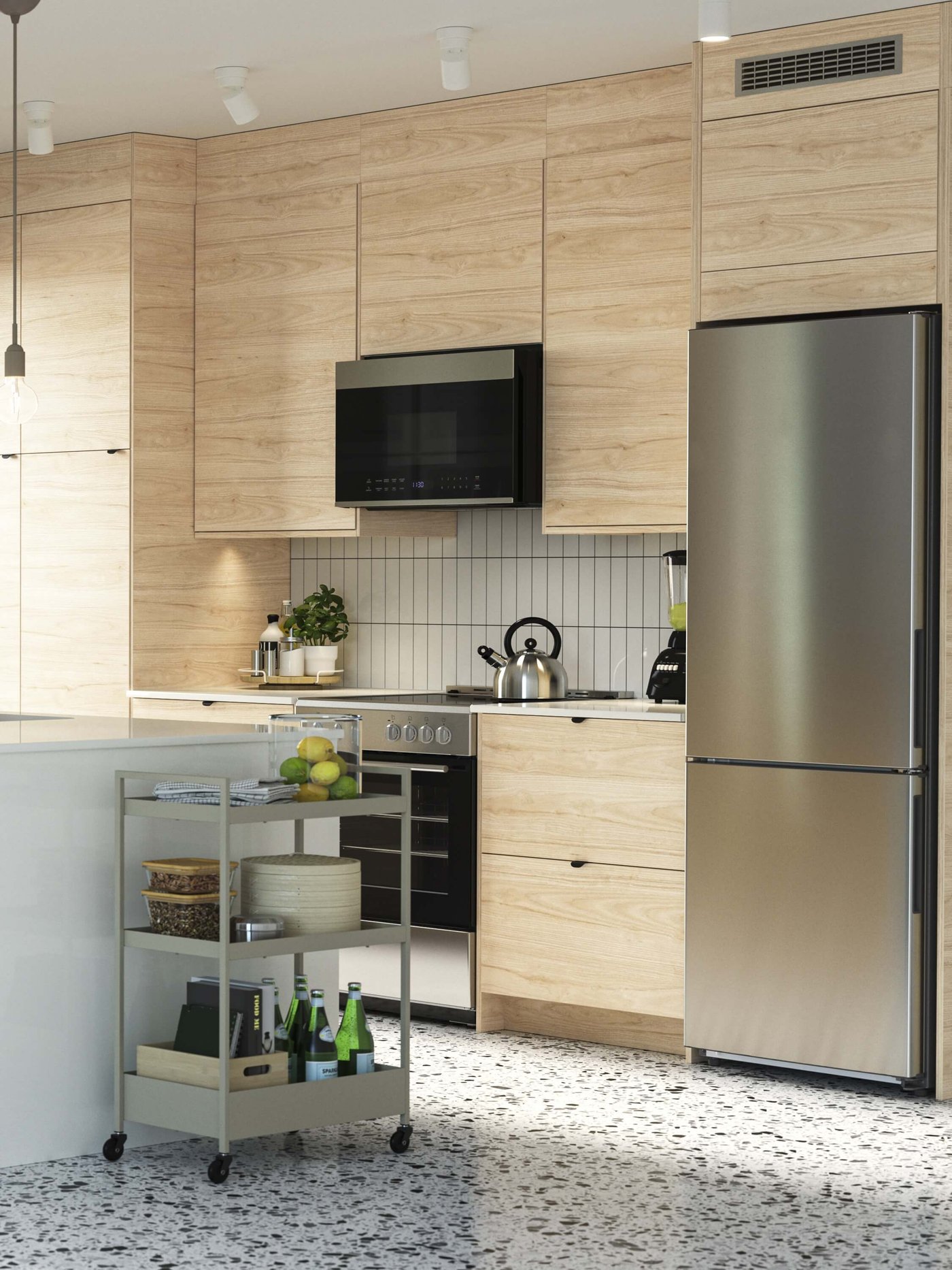 Modern kitchen with light wood cabinets, stainless steel fridge, built-in oven and rolling cart.