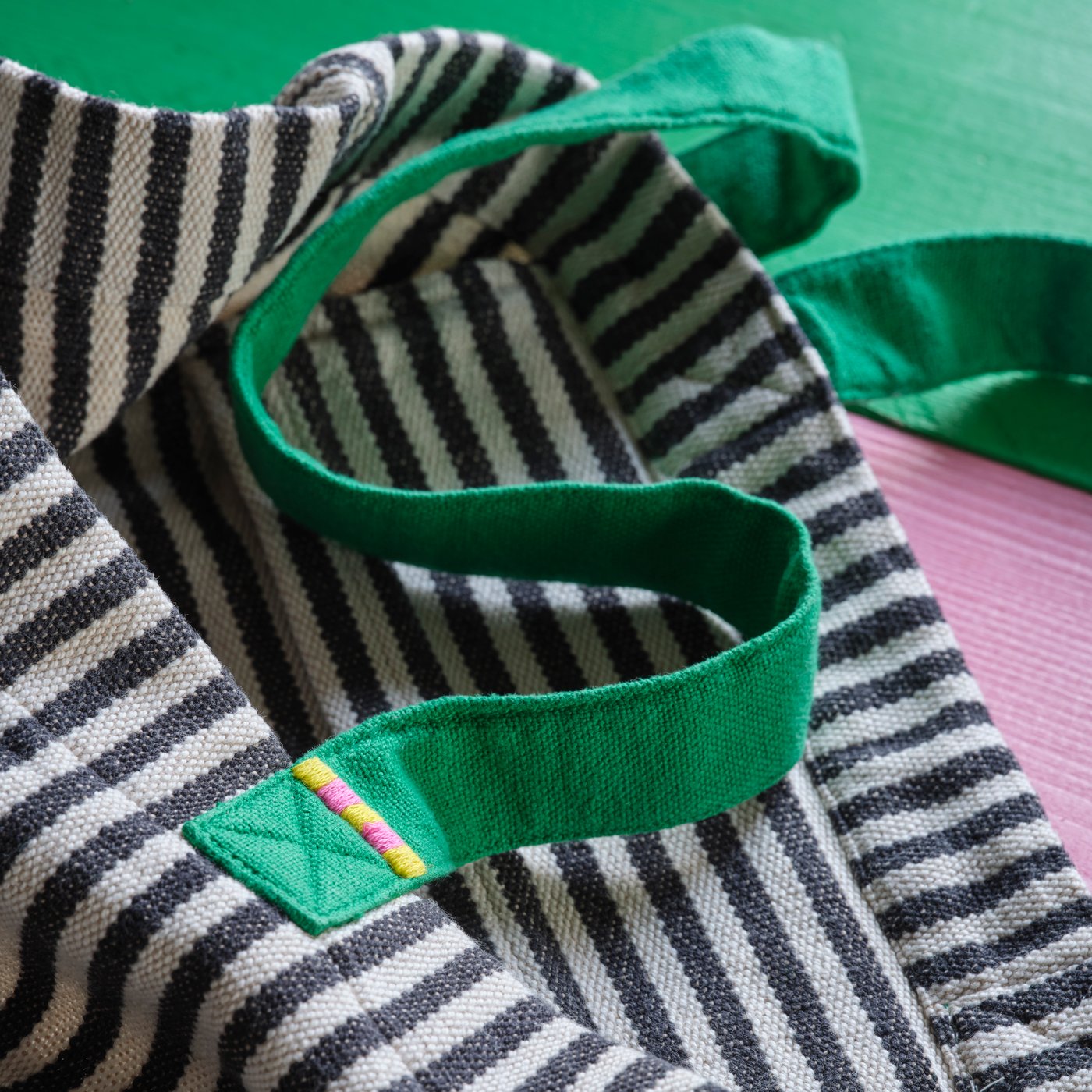 A close-up of a black and white striped MÄVINN tote bag in cotton/yarn with green handles and an embroidered detail.