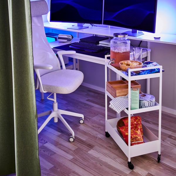 A white NISSAFORS trolley holding snacks and lemonade is next to an office chair and shelves with two computer screens.