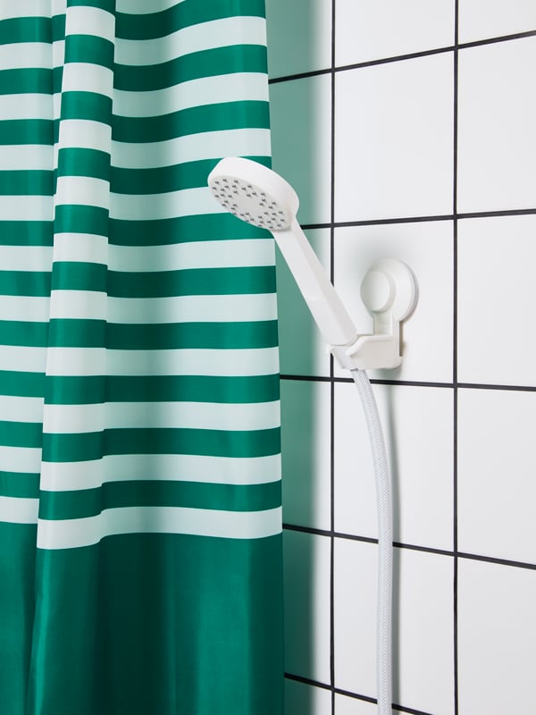 A white and blue VATTENSJÖN shower curtain with a fish motif and a green plant standing next to the shower in a bathroom.