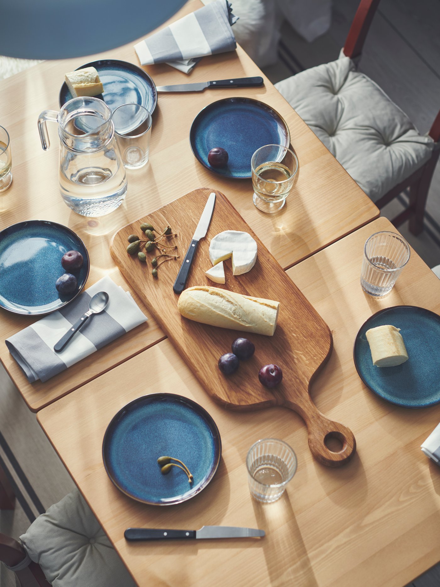 Cocina con 2 mesas rectangulares de pata de gata PINNTORP que sostienen 4 platos azules GLADELIG y una tabla de cortar ARTISTIK.