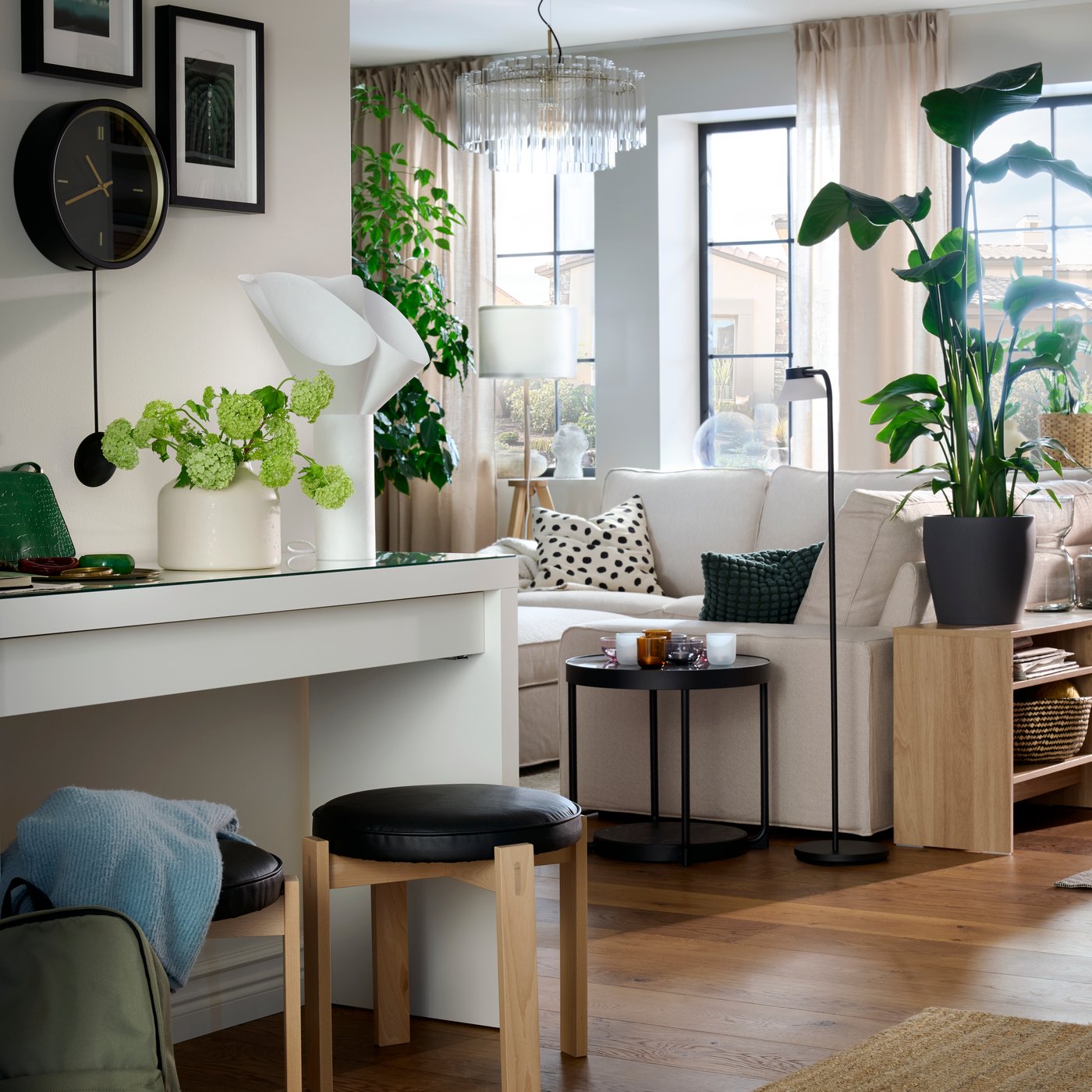 A bright hallway and living room centred around a KIVIK sofa surrounded by plants and textiles, and flanked by large windows.