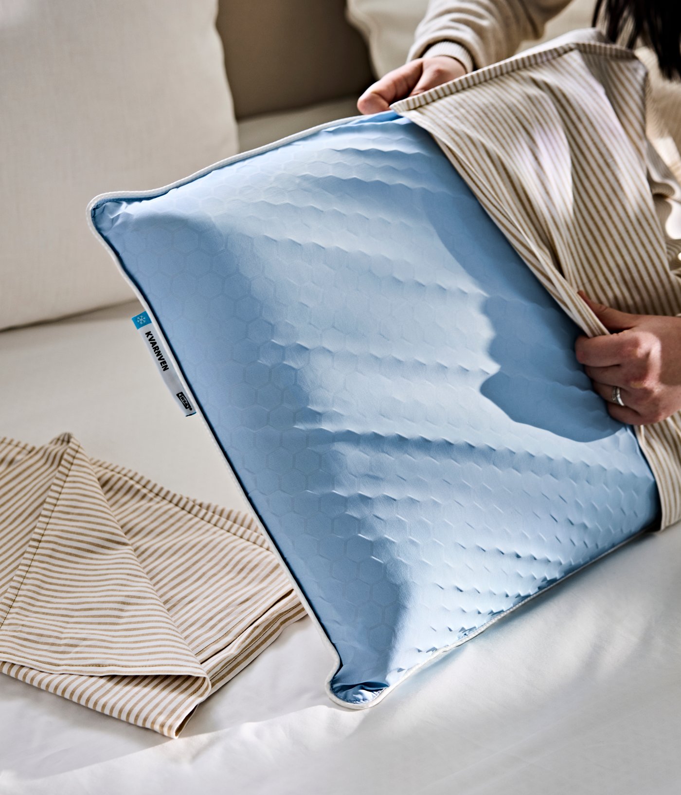 A person is putting on a striped LAGERPOPPEL pillow case on a KVARNVEN ergonomic pillow.