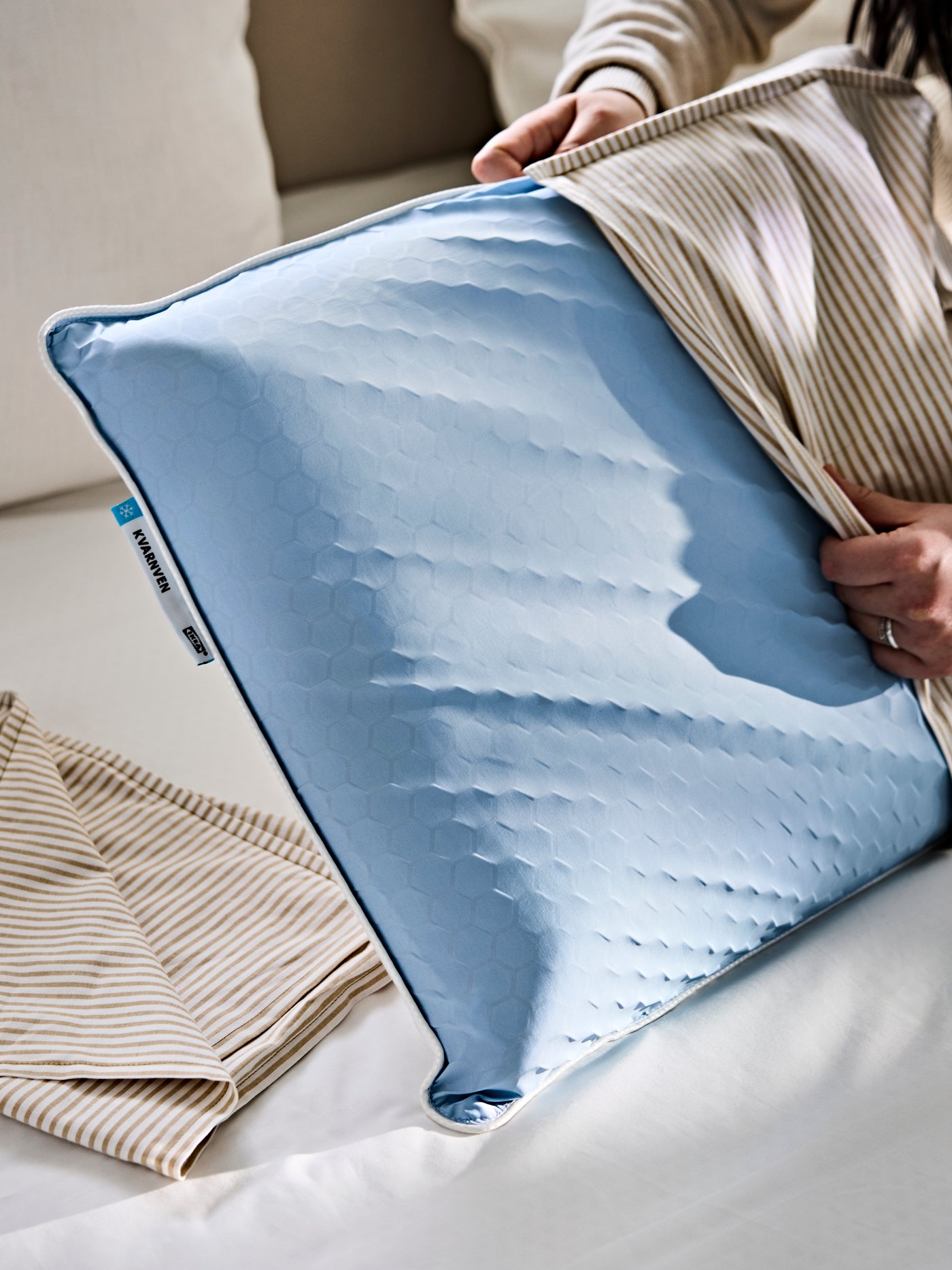 Eine Person bezieht einen gestreiften LAGERPOPPEL-Kissenbezug über ein ergonomisches KVARNVEN-Kissen.