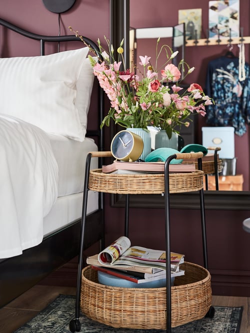 Schlafzimmer mit Bettrahmen aus Stahl, Bettbezug und Kissenbezügen, Trolley aus Stahl und Rattan, Tischuhr, Regal mit Haken. 