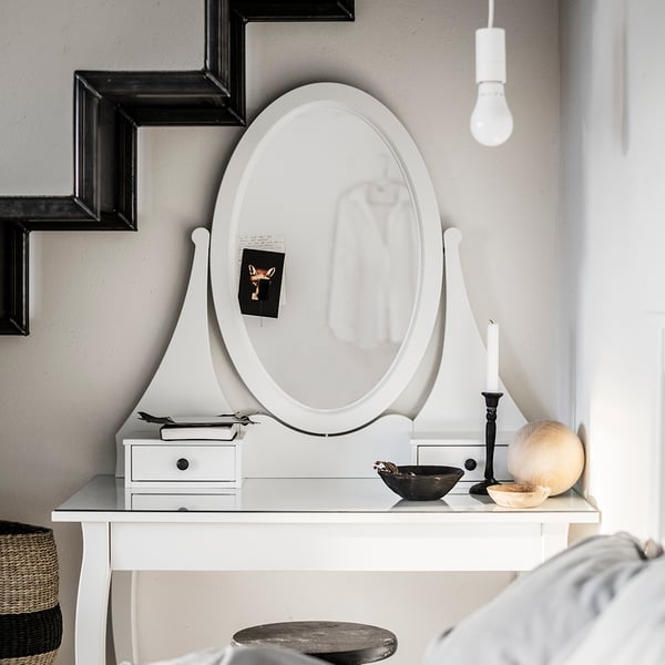 A black KORNSJÖ cabinet with a large, round mirror, displaying decorative objects and a white lamp placed above it.
