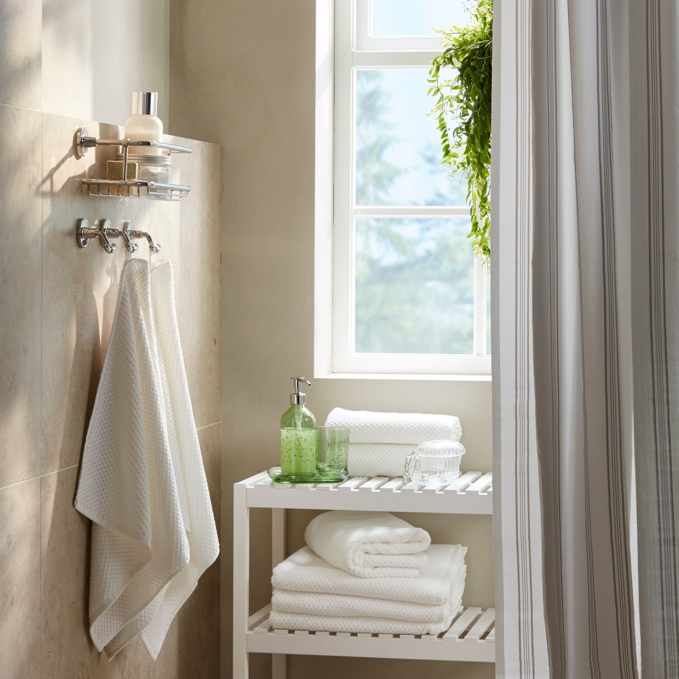 A bathroom corner has a GROSSJÖN 3-piece bathroom set in green floral-motifed glass on a white bench by stacked white towels.