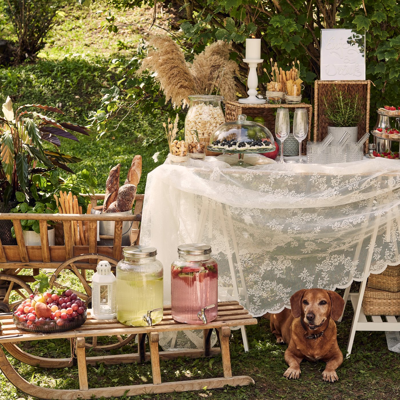 Aus einem alten Schlitten, einem Handkarren aus Holz, zwei Böcken und einer Holzplatte mit Tüll wurde eine Selbstbedienungsbar mit Getränkespendern, Etageren und Körben mit Snacks gebaut