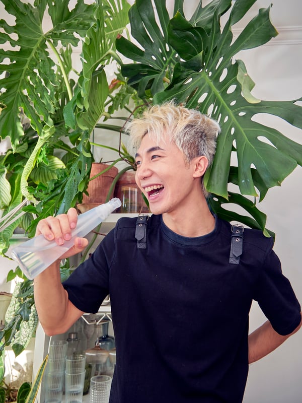 A man is playfully singing into a TOMAT spray bottle, as if it were a microphone.