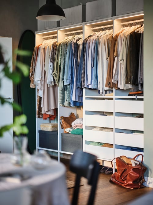 Une salle de lavage avec une armoire-penderie, des vêtements suspendus sur des cintres, une baguette lumineuse à DEL, des bacs avec couvercle, une suspension et une table. 