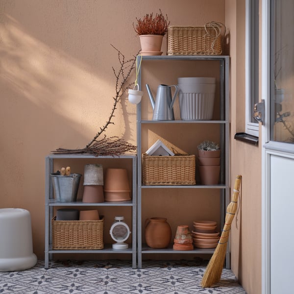 A tall HYLLIS shelving unit stands next to a shorter HYLLIS shelving unit on a balcony. They hold baskets and plant pots.
