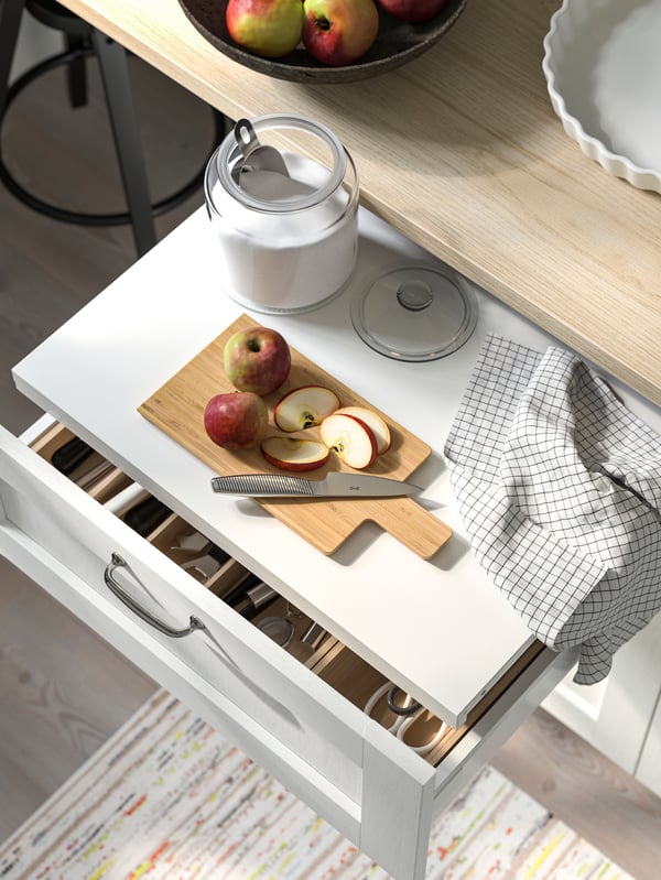 An UTRUSTA pull-out shelf has been pulled out in a drawer with a white ENKÖPING front and a chrome-plated ENERYDA handle.