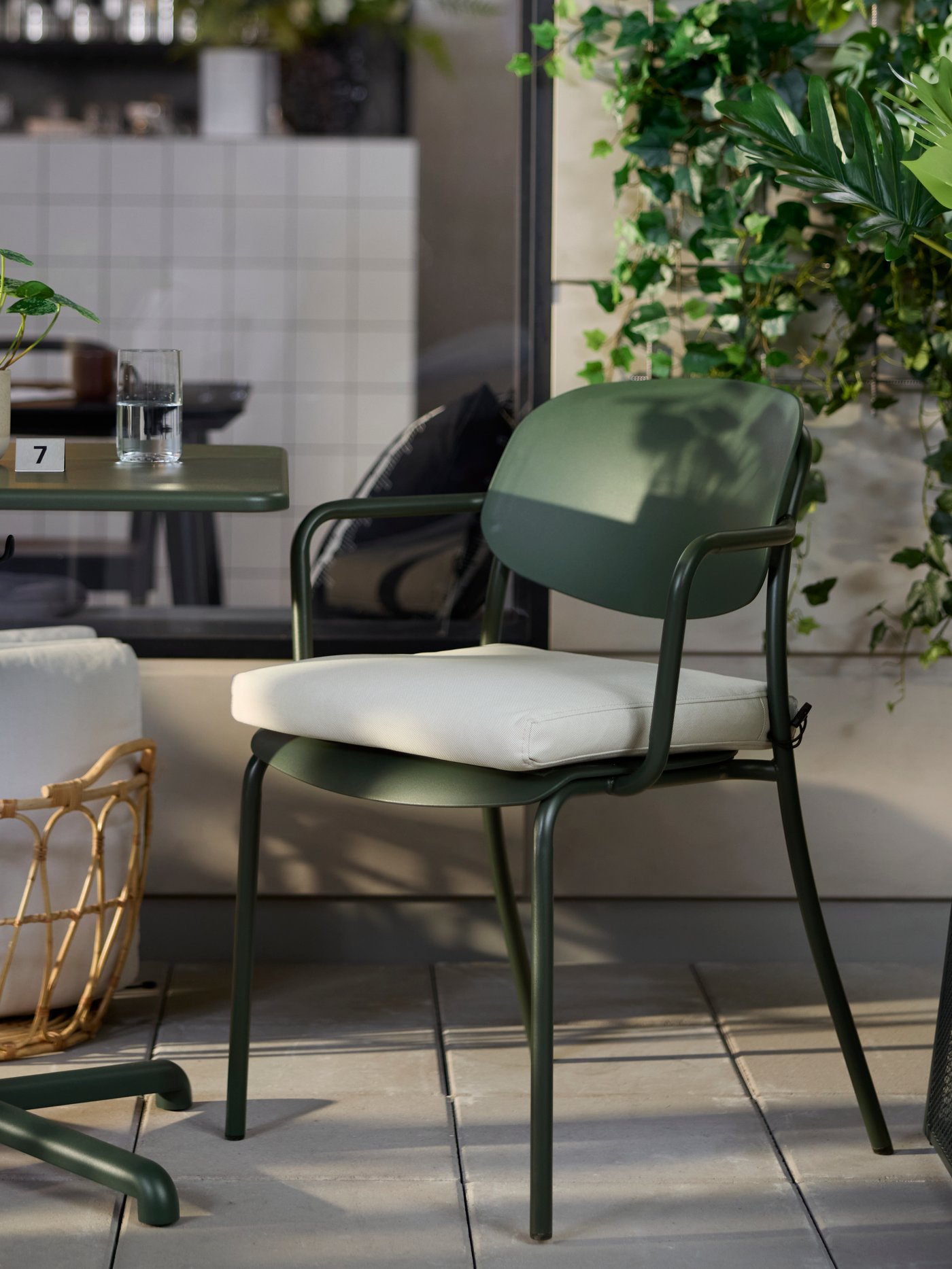 Café outdoor seating with deep green VISINGSÖ table and armchair, surrounded by greenery and outdoor décor.