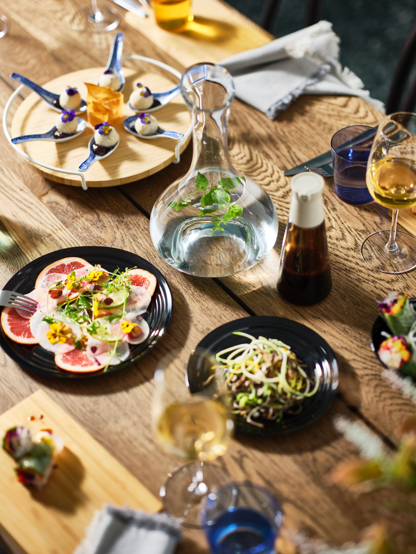A MÖRBYLÅNGA table in dark oak veneer is set with different coloured plates and festive dishes and a STORSINT carafe.