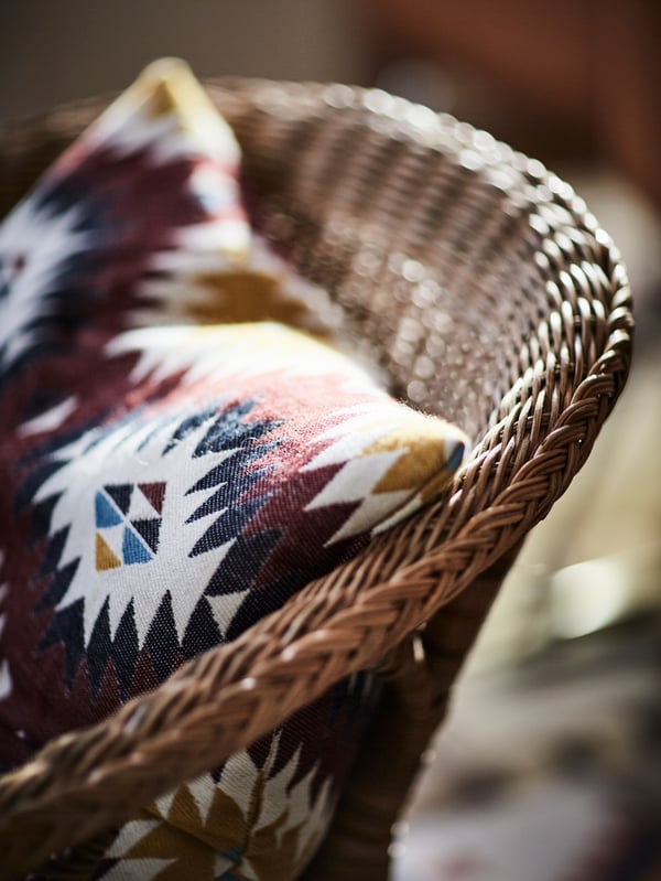 Close-up of the AGEN armchair in rattan and bamboo with a cushion resting on its seat.