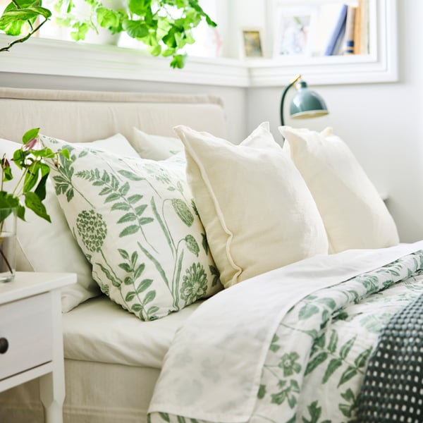 A bed, neatly made with NÅLBJÖRNBÄR duvet cover and pillow cases and decorative pillows in white.