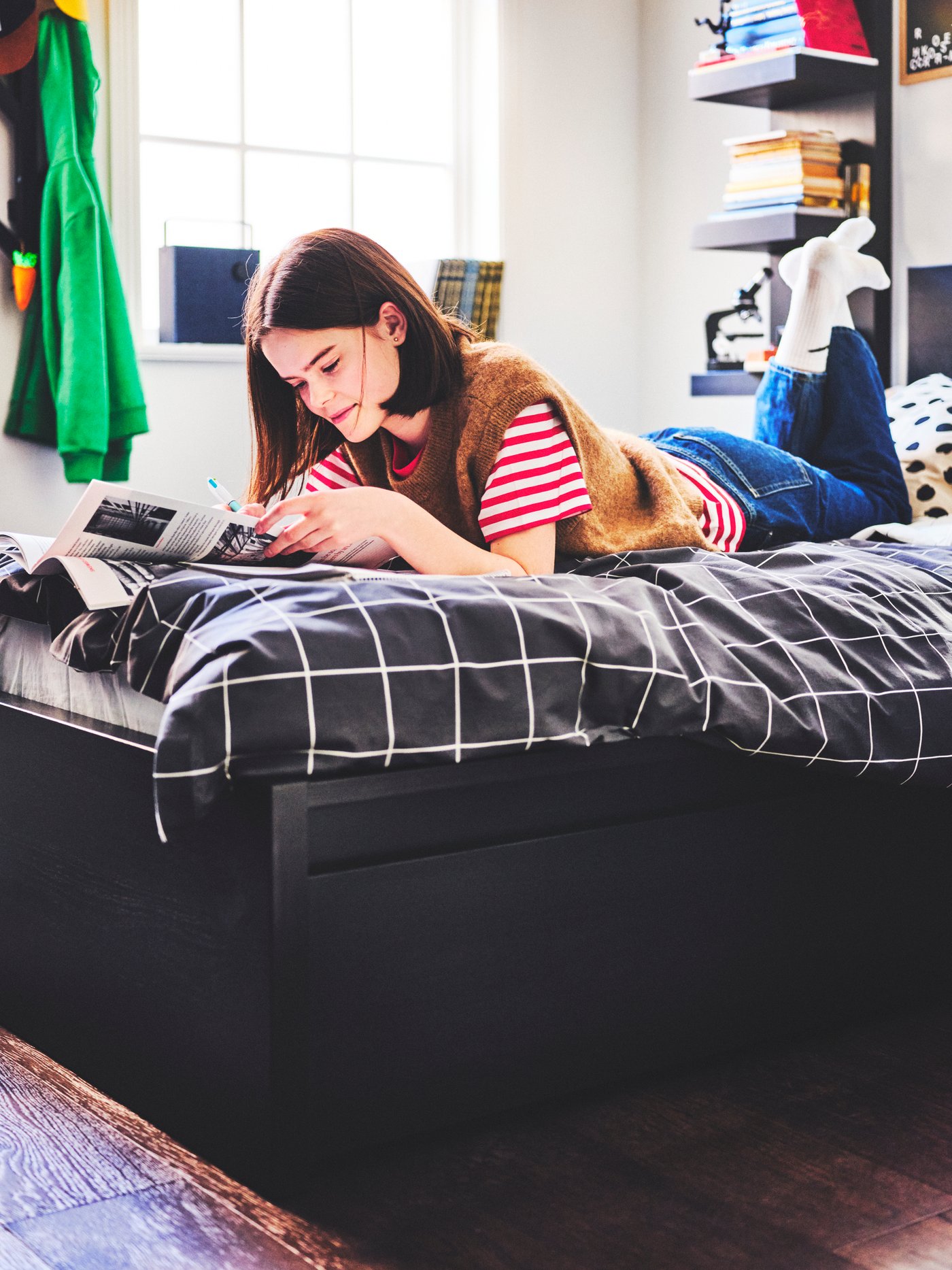 A person reading while lying on a black MALM bed with two storage boxes dressed in a VITKLÖVER duvet cover and pillowcase.