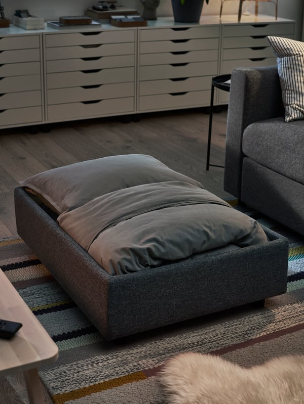 Bedding stored inside a footstool, in Gunnared medium grey, with ALEX drawer units in the background.