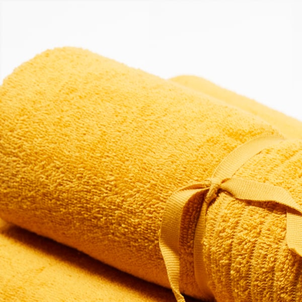 A top view of a rolled-up yellow VÅGSJÖN towel that is tied together with a yellow ribbon and placed on top of another yellow VÅGSJÖN towel.