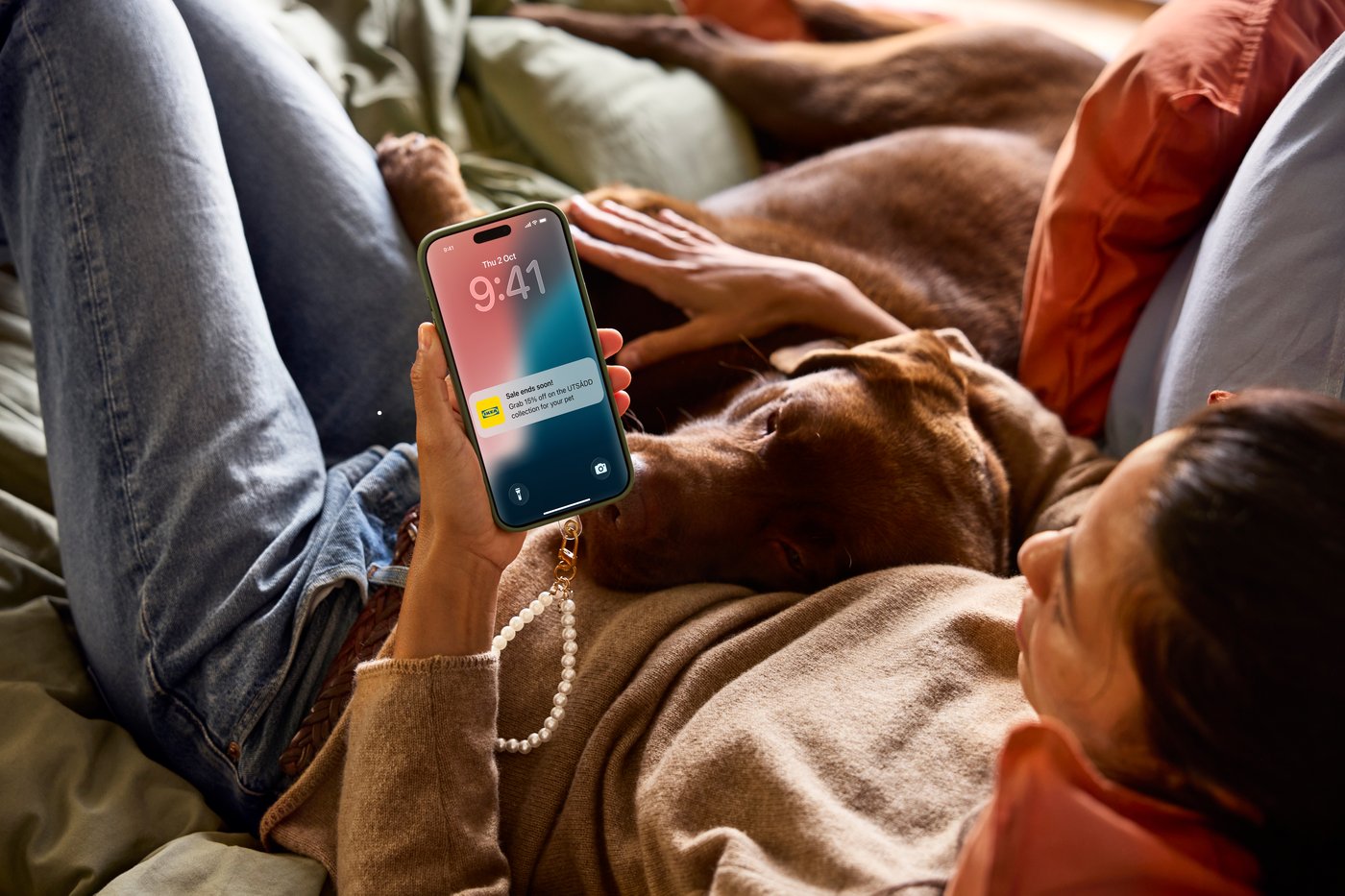 Kobieta leżąca na łóżku z psem obok, trzymająca telefon z powiadomieniem na telefonie