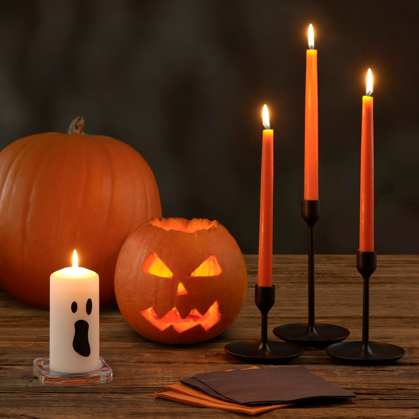 Table with carved pumpkin and lit candles.