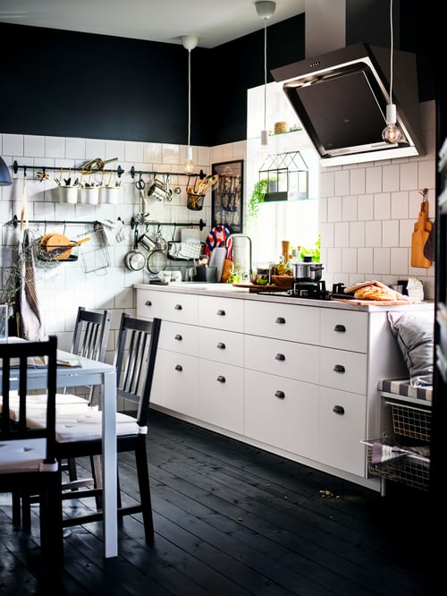 Kitchen with white base cabinets with three drawers, a wall mounted extractor hood, a grey worktop, a table, and chairs.