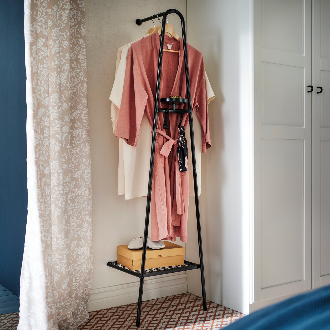 A PAX/TYSSEDAL wardrobe combination with a black ÄLGANÄS wall-anchored clothes rack with shoe storage holding clothes by it.