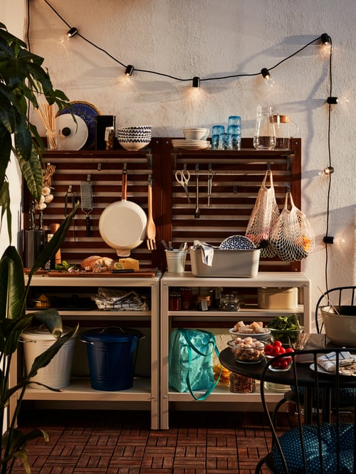 Étagère intérieure/extérieure KOLBJÖRN sur un patio avec des articles de jardinage et de cuisine extérieurs sur ses étagères et son plan de travail en acier.