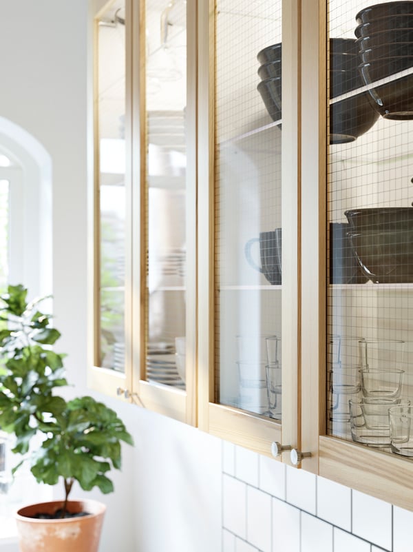 Wall cabinets with four ash and glass TORHAMN doors that store tableware.