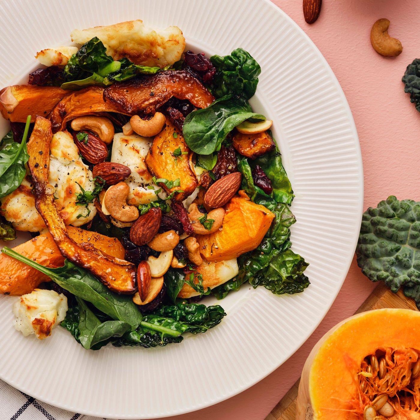 A pumpkin salad with butternut squash, black kale, goat cheese, and a MUNSBIT mix of roasted nuts/berries on a white plate.