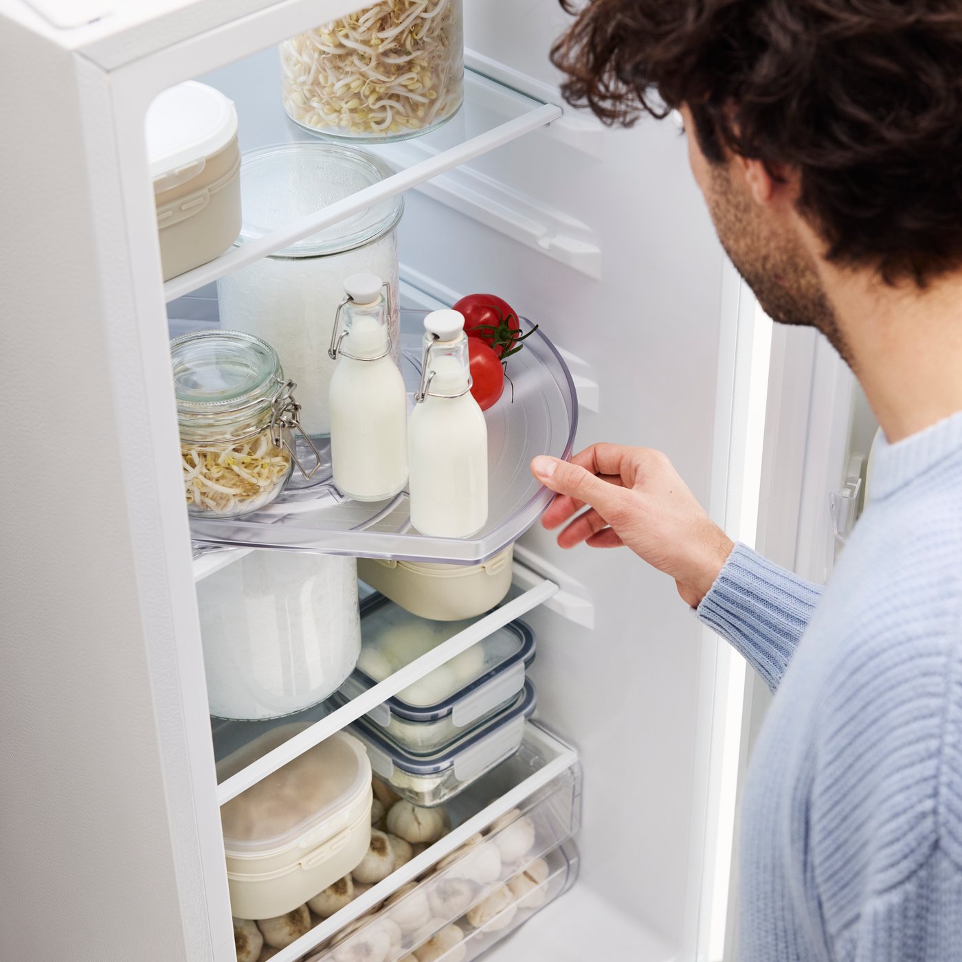 Henkilö kääntää jääkaapissa olevaa SNURRAD-tarjotinta, jolla on maitopulloja ja säilytyspurkkeja.