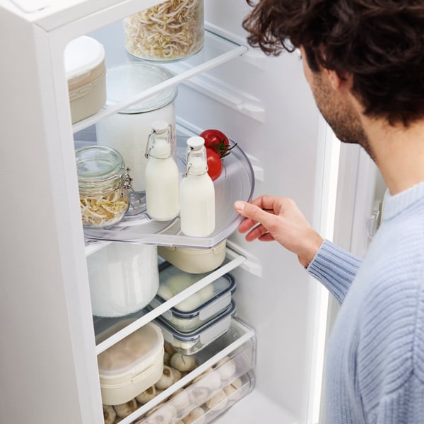 A person opens a fridge, and pulls out a SNURRAD turntable, containing bottles of milk, leftovers in a jar and fresh tomatoes.