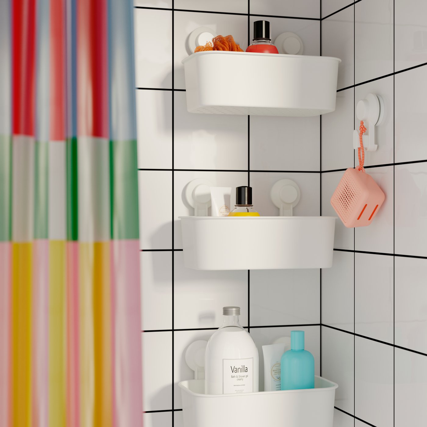 Three TISKEN baskets with suction cups hanging vertically in a row near a colourful shower curtain and a pink WiFi speaker.